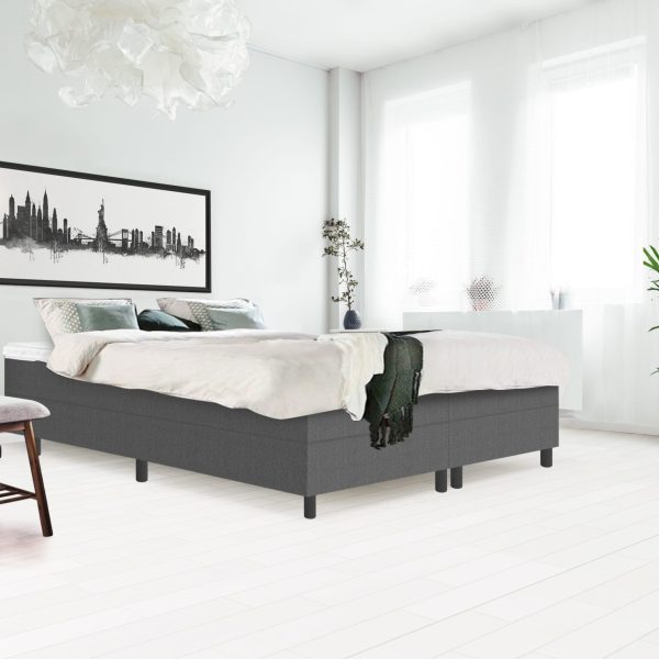 Side angle of bright bedroom interior with gray bench standing next to a wooden bed with white bedding, gray coverlet and pillows