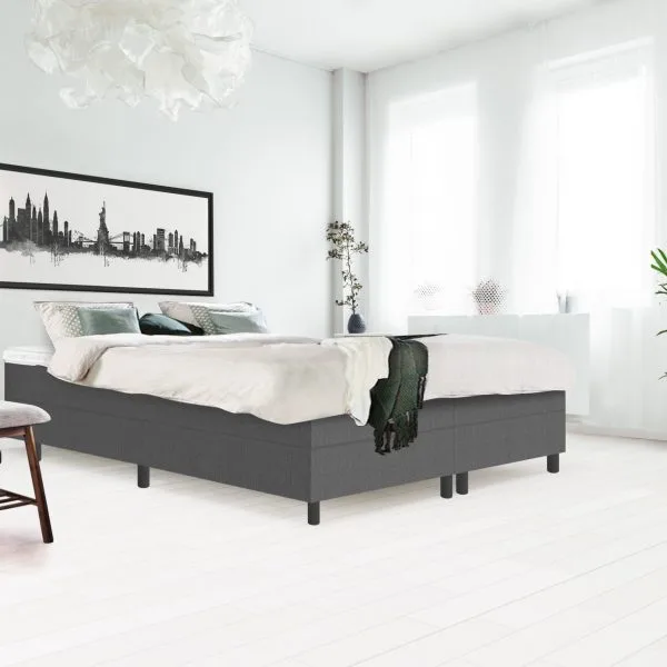 Side angle of bright bedroom interior with gray bench standing next to a wooden bed with white bedding, gray coverlet and pillows