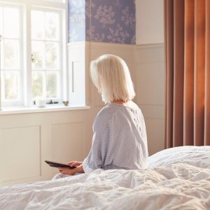 Vrouw zit op rand van bed naar buiten te kijken