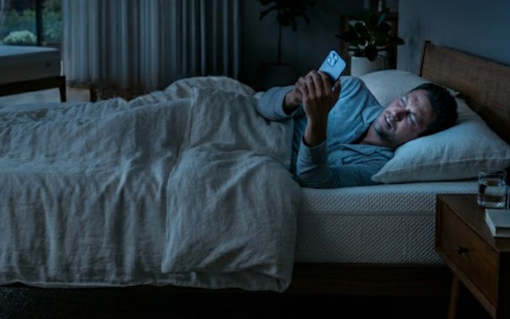 Man ligt in bed en scrolt op zijn telefoon
