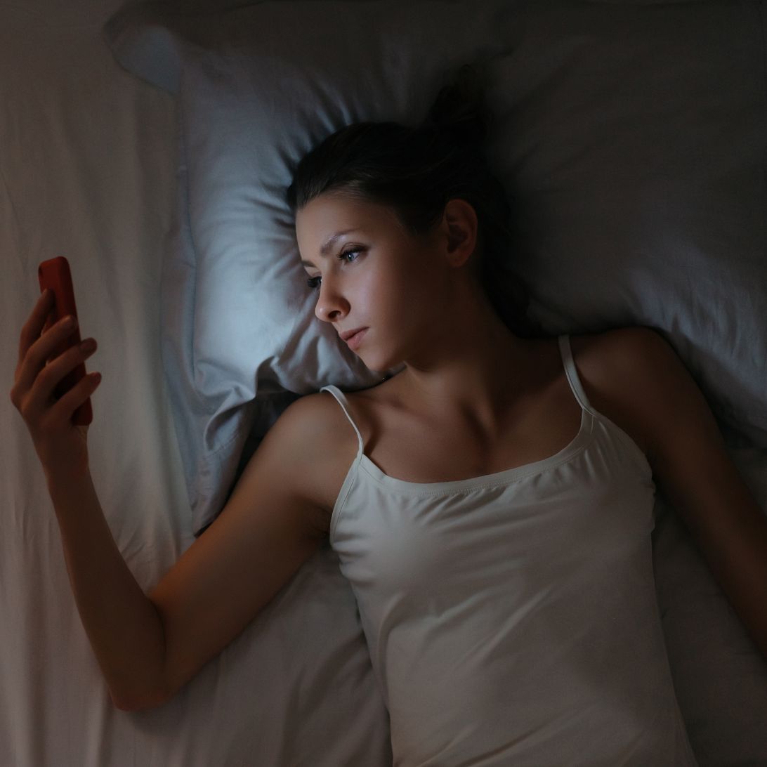 Vrouw zit op telefoon voor het slapen, blauw licht schijnt op haar gezicht