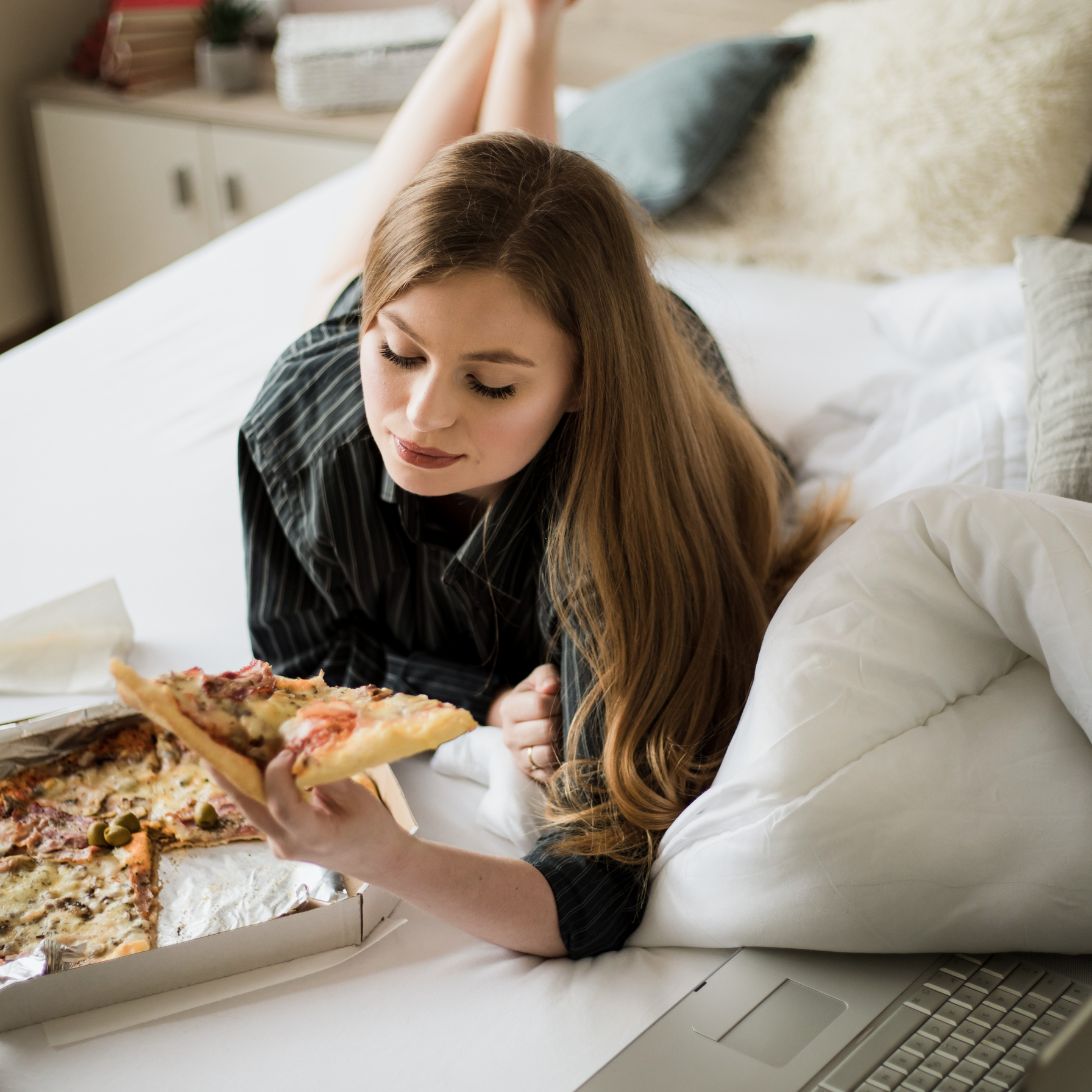 Vrouw is pizza in bed aan het eten voor het slapengaan