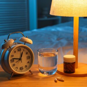 Melatonine, glas water, wekker en lamp op nachtkastje