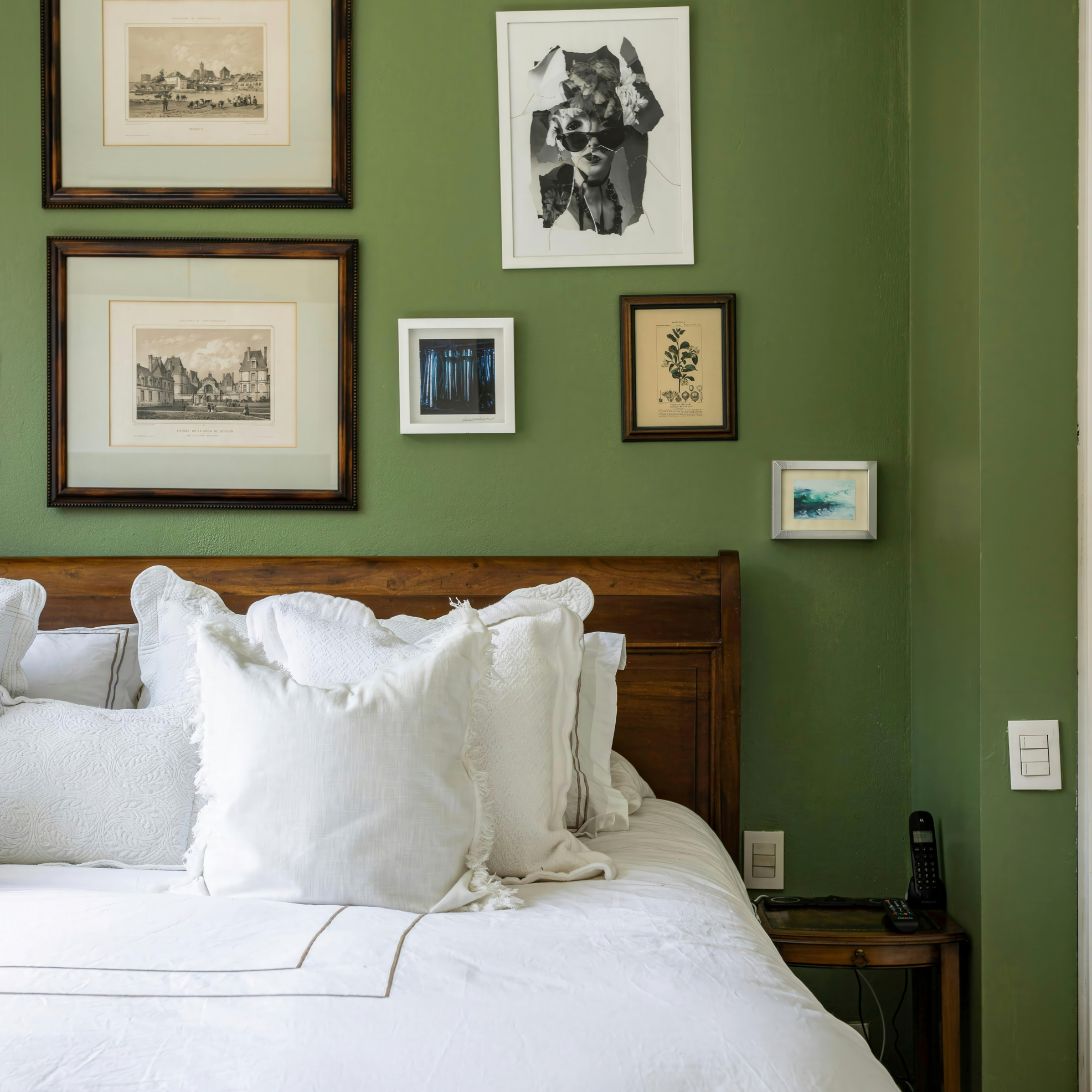 Slaapomgeving met opgedekt bed, groene muur en schilderijen
