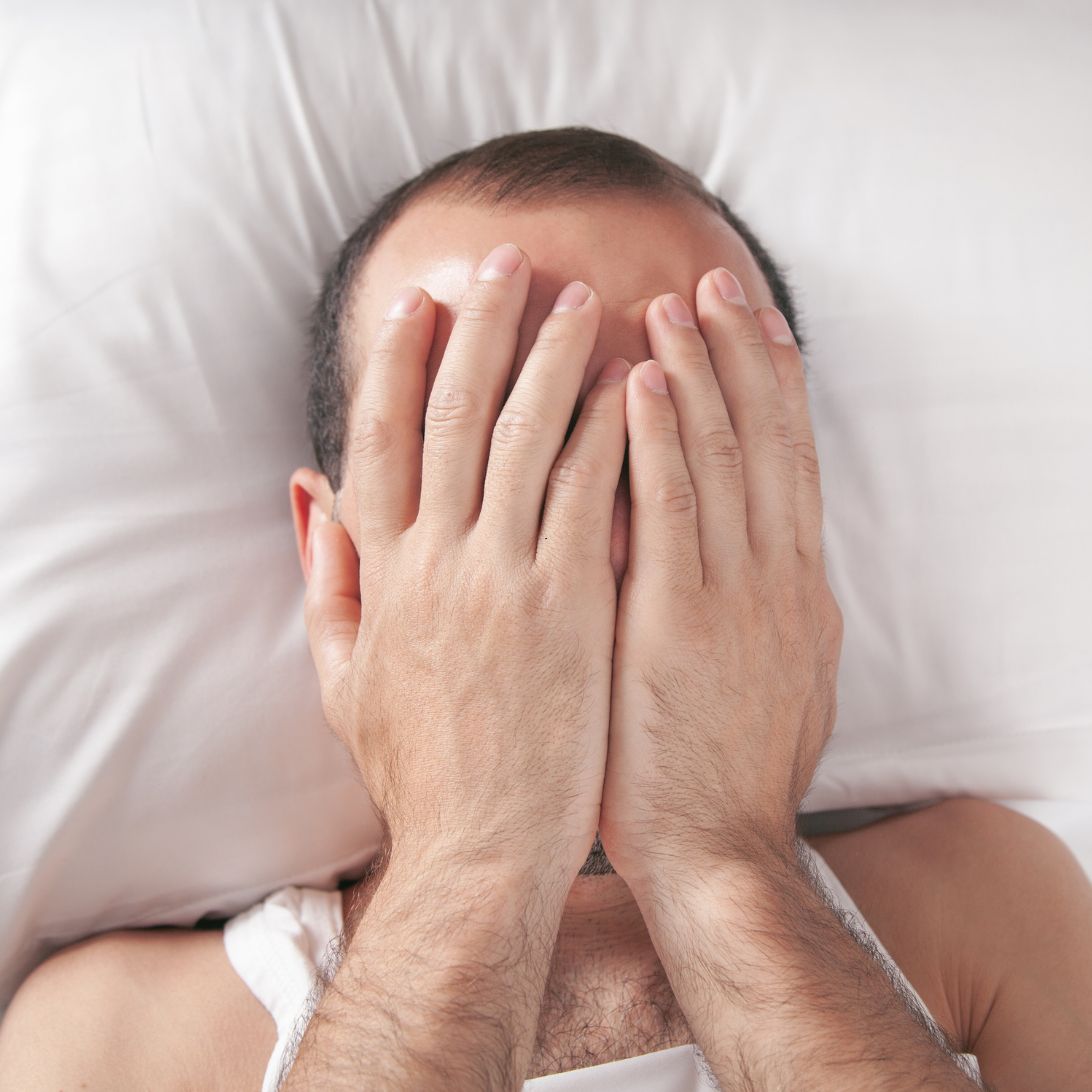 Man is zijn slaapproblemen aan het herkennen doordat hij midden in de nacht wakker ligt, heeft handen op ogen. 