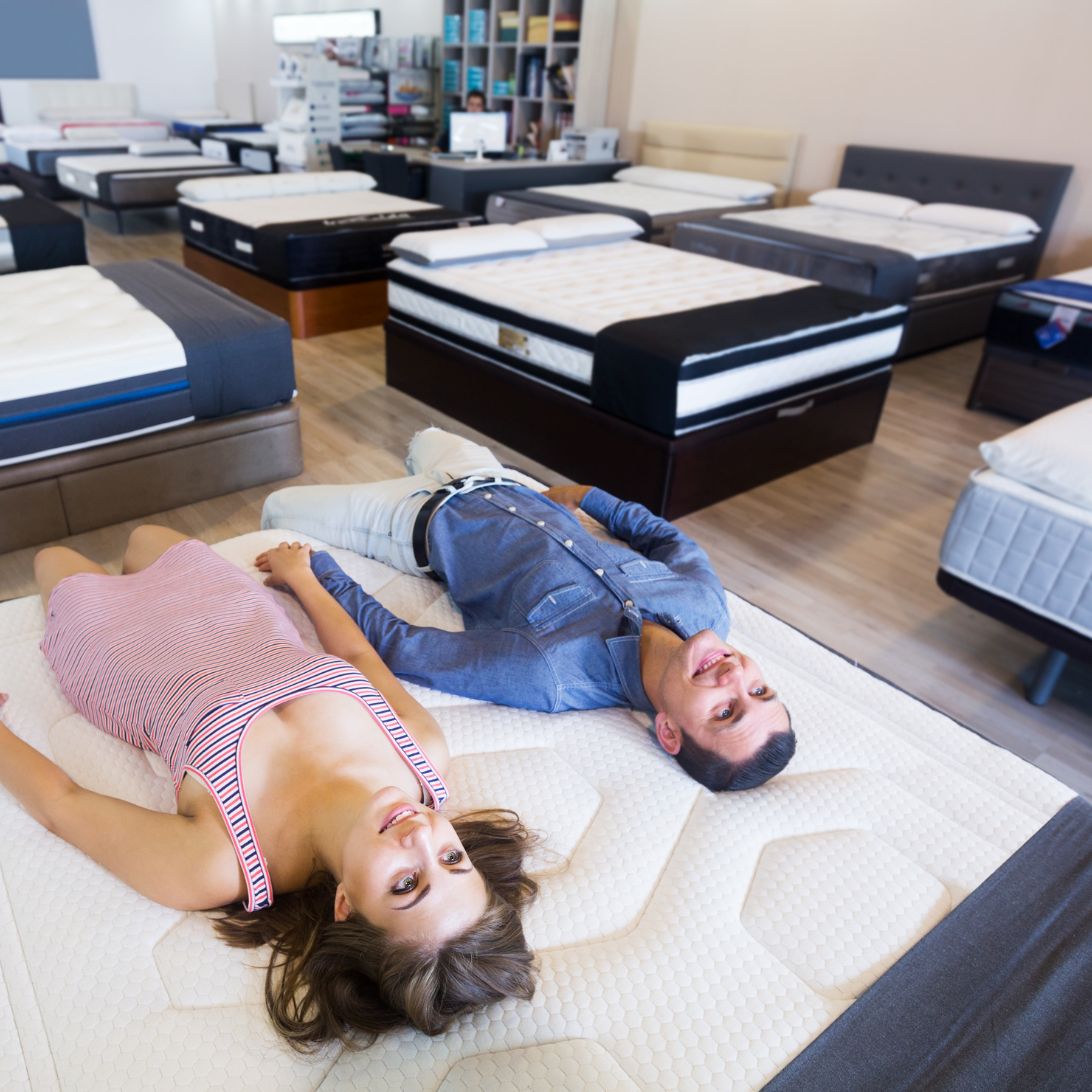 Man en vrouw testen verschillende soorten matrassen in winkel